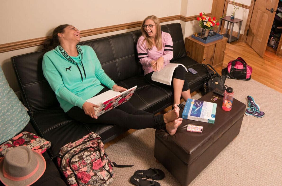 Two female students laugh while sitting on a futon in a dorm room 